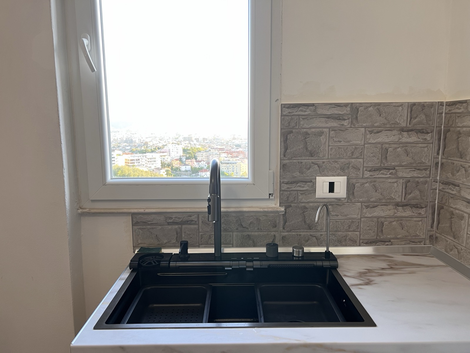 Kitchen sink set beneath a window framing the Tirana skyline